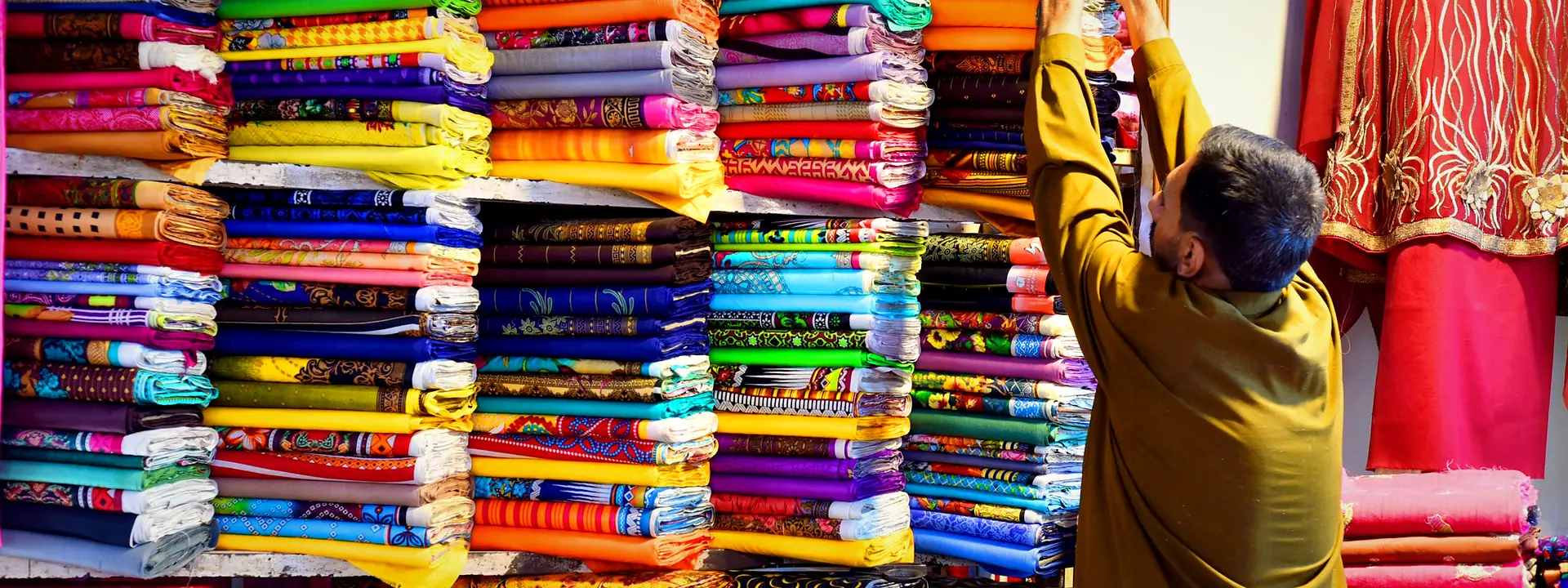 A vendor arranging colourful stacks of fabric at a Pakistani market