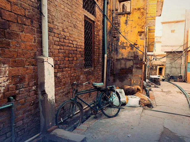 An old bicycle leaning on a weathered brick wall in a quiet Chiniot alley
