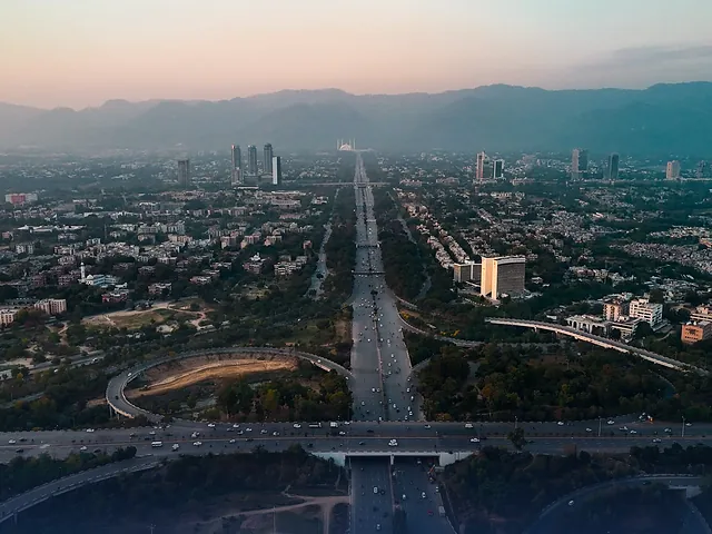 Aerial view of Islamabad at dusk, with highways, buildings and the Margalla Hills