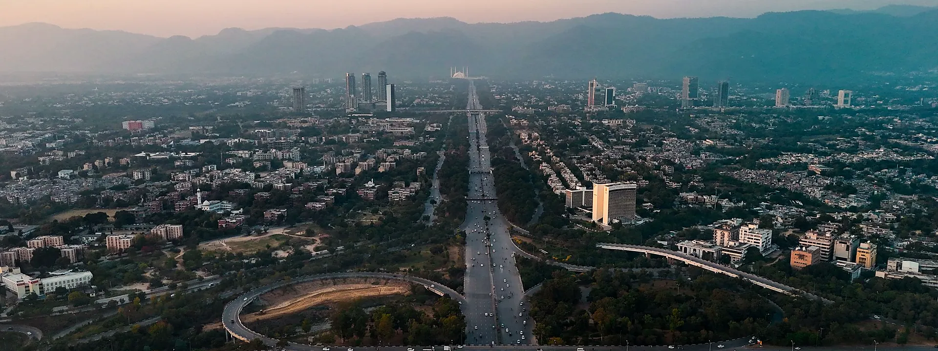 Aerial view of Islamabad at dusk, with highways, buildings and the Margalla Hills