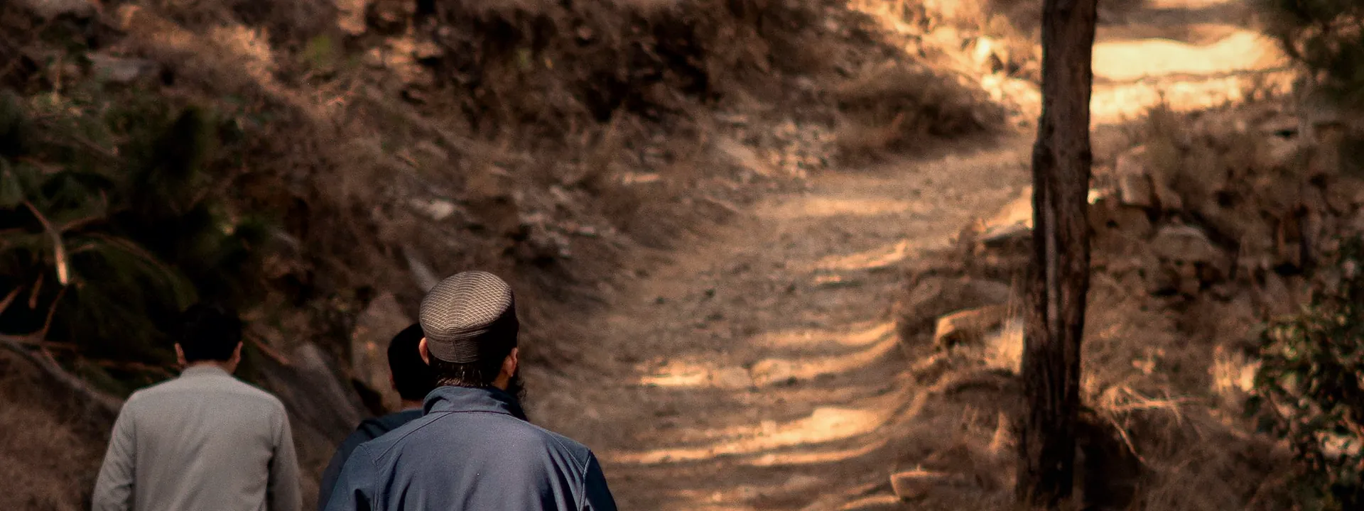 Two walkers on a sunlit trail through the hills of Mansehra