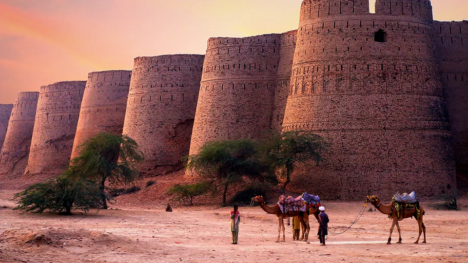 Derawar Fort's towers at sunset with camels in the Cholistan desert, Punjab