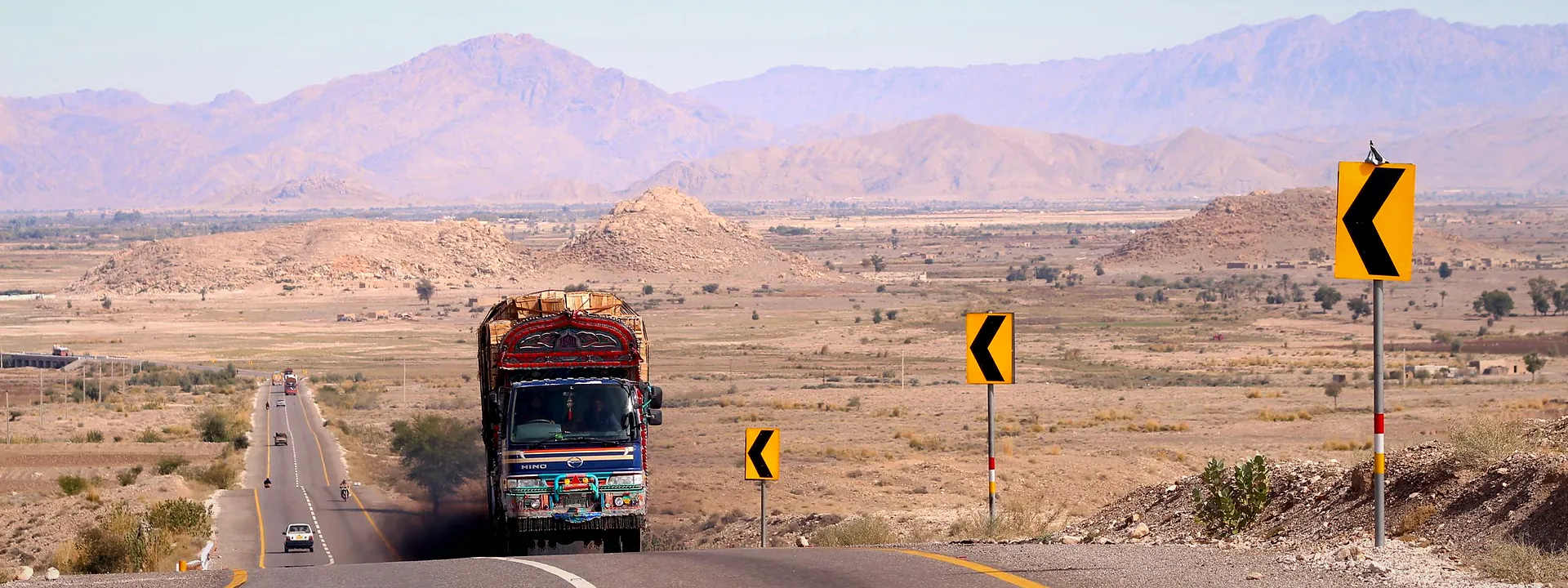 A colourful truck on a winding road through the arid mountains of Balochistan